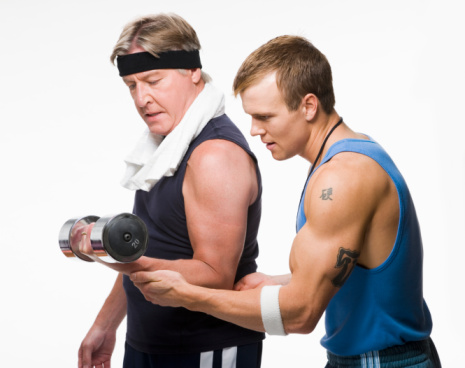 Fitness trainer helping mature man during exercising with weights