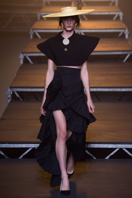 Simon Porte Jacquemus: người mẫu mặc áo crop top đen, chân váy xòe nhiều lớp màu đen  và mũ cói.