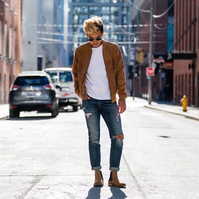 chàng trai mặc áo bomber nâu, áo thun trắng, quần jeans rách và giày chelsea boots nâu.